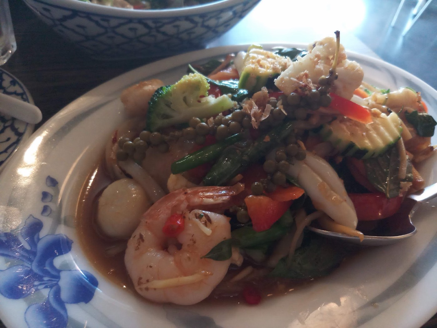 A stir-fry of prawns, quail eggs, broccoli and green peppercorns in sauce on a white plate with blue flowers