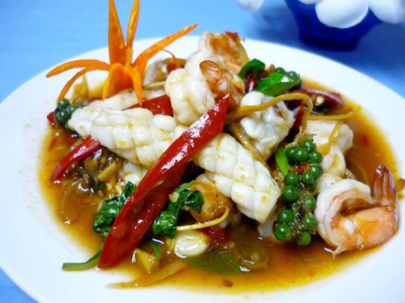 A plate of stir-fried squid, prawns, long red chillies and green peppercorns in a glossy sauce