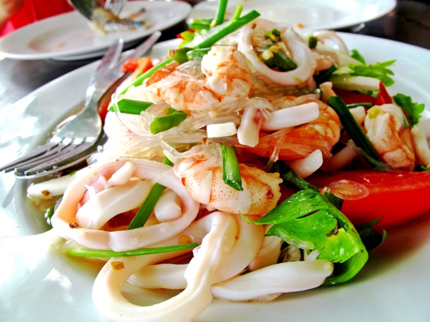 A salad of squid rings, prawns, tomato, spring onion and herbs on a white plate